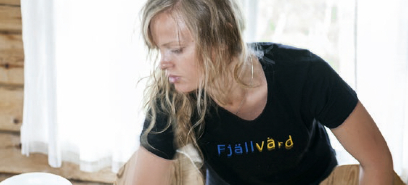 Bemanningsanställd kvinna torkar ett bord. Hon har en t-tröja med texten Fjällvärd på.